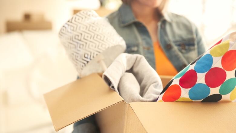 A woman carries a cardboard box with a lamp and blanket inside.