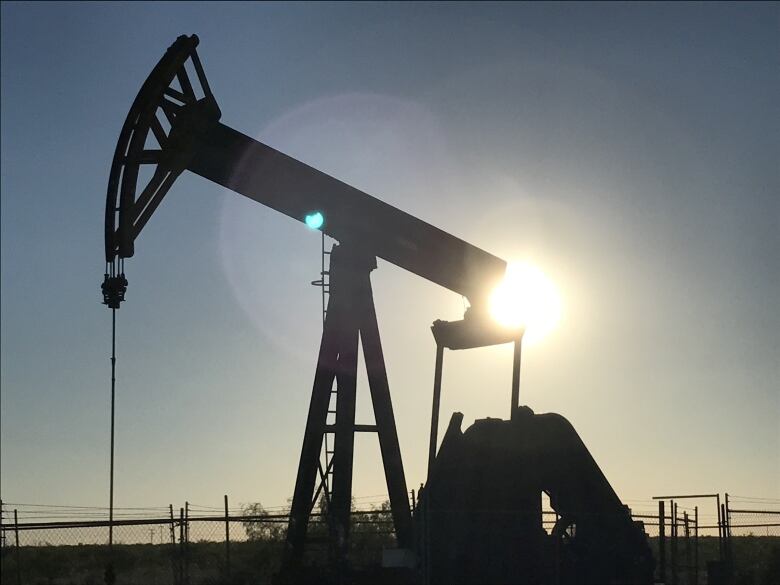 An image shows a petroleum pumpjack against a dusky sky in close up.