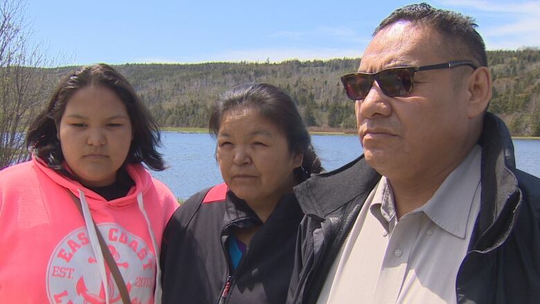 A man, woman and teenage girl stand in front of a river. 