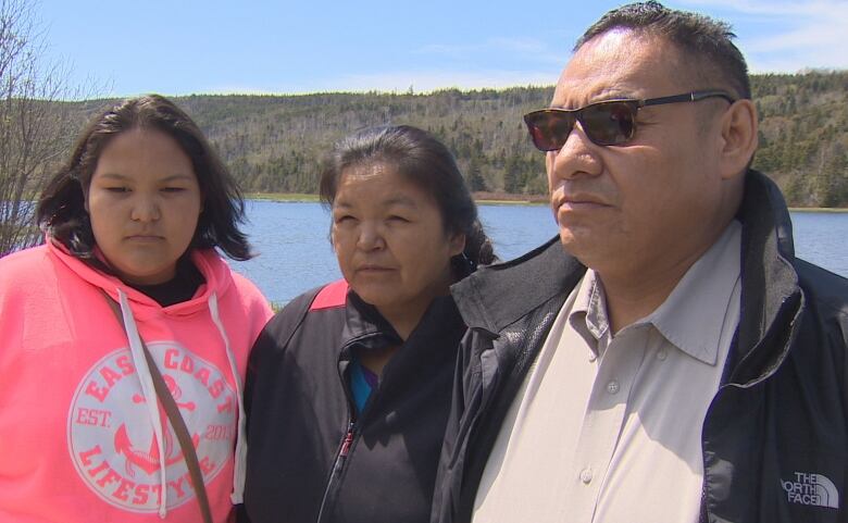 A man, woman and teenage girl stand in front of a river. 