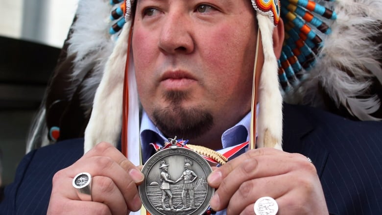 Pine Creek First Nation Chief Derek Nepinak holds a treaty medallion while wearing a headdress.