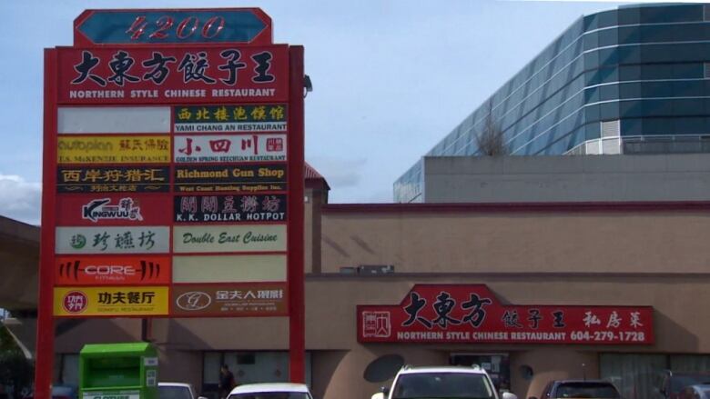 Lots of signs in Chinese on a billboard in front of what looks like a strip mall.