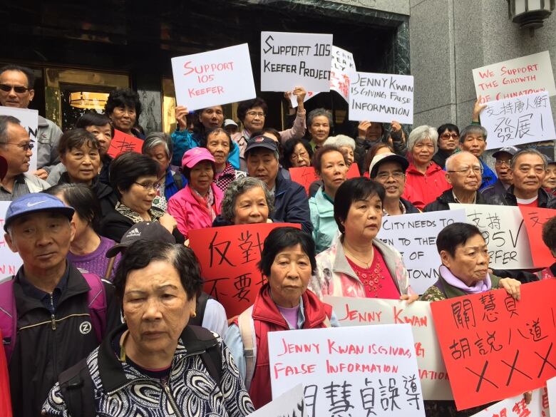 A group of predominantly Chinese women stand holding signs that say support 105 Keefer.