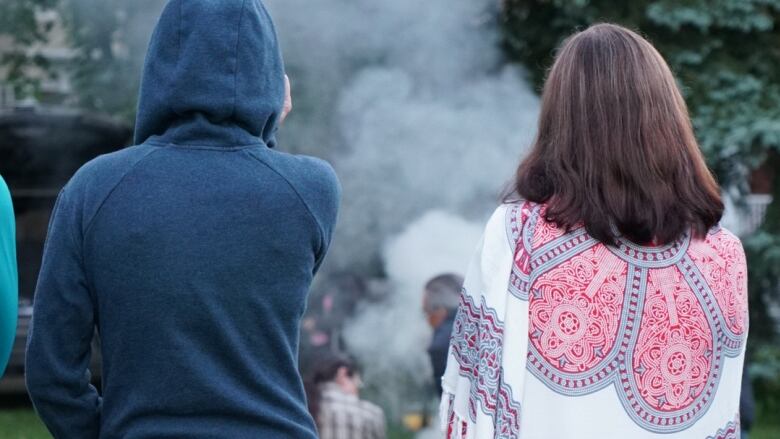 Two individuals - a man and a woman - look at a sacred fire with their backs to the camera.