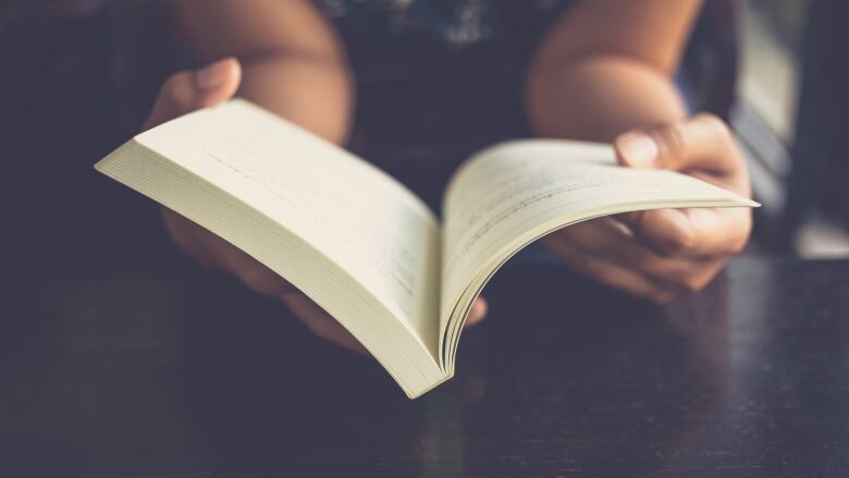 Hands holding a paperback book open.