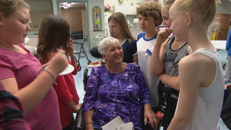 Jodi Grant sits in a wheelchair surrounded by happy Grade 6 students.