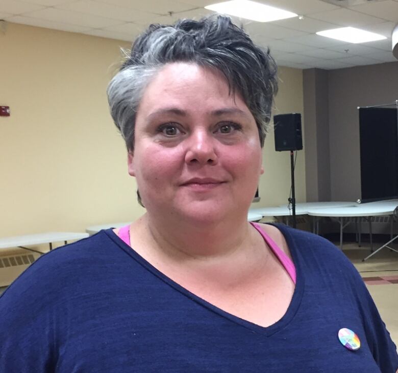  A woman with short grey hair looks at the camera. She is wearing a purple t-shirt. 