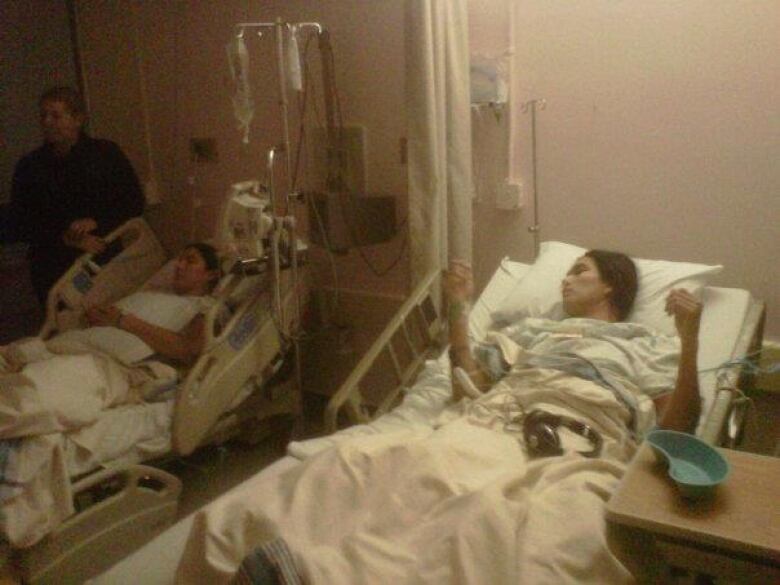 Two people lie in hospital beds, with a person standing close by.