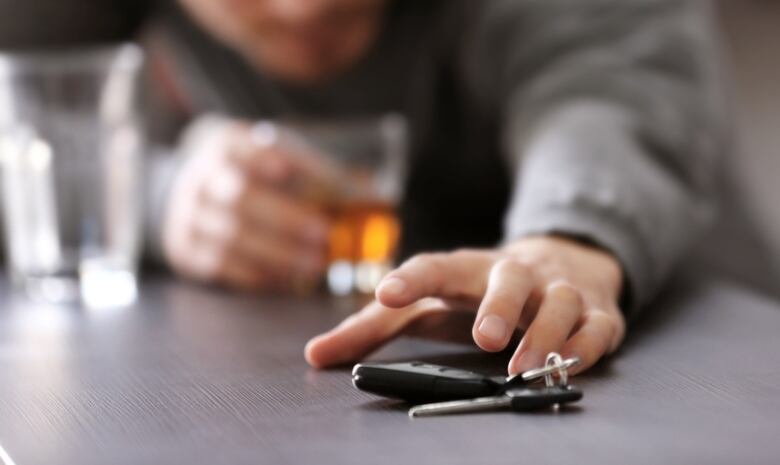 Photograph of a man reaching for keys while drinking whiskey 