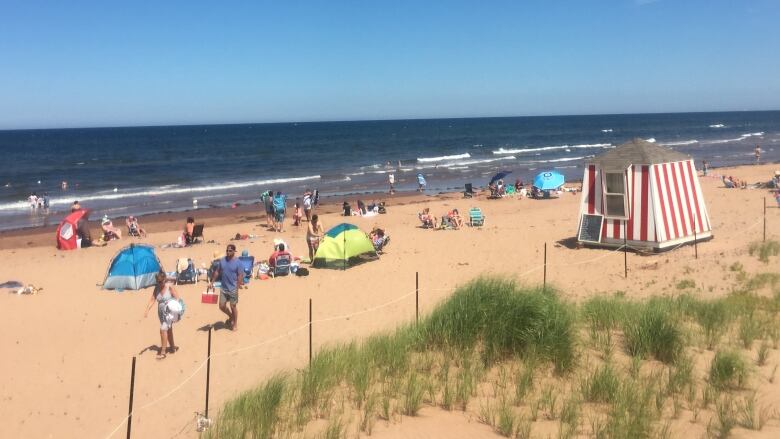 A busy beach in PEI National Park with a red and white striped shelter in the foreground