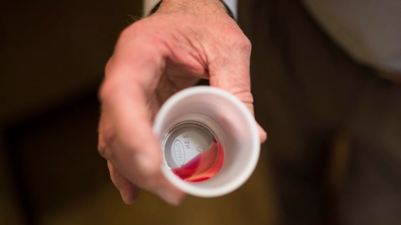 A hand holding a small plastic cup containing some red liquid.