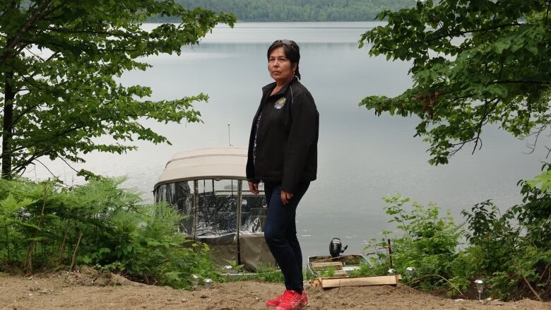 A woman stands in front of a water body.