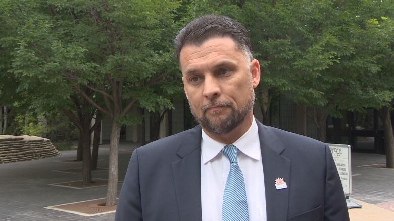 A man wearing a black suit with a blue tie outside. 