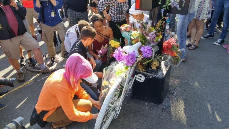 People place flowers on a white ghost bike