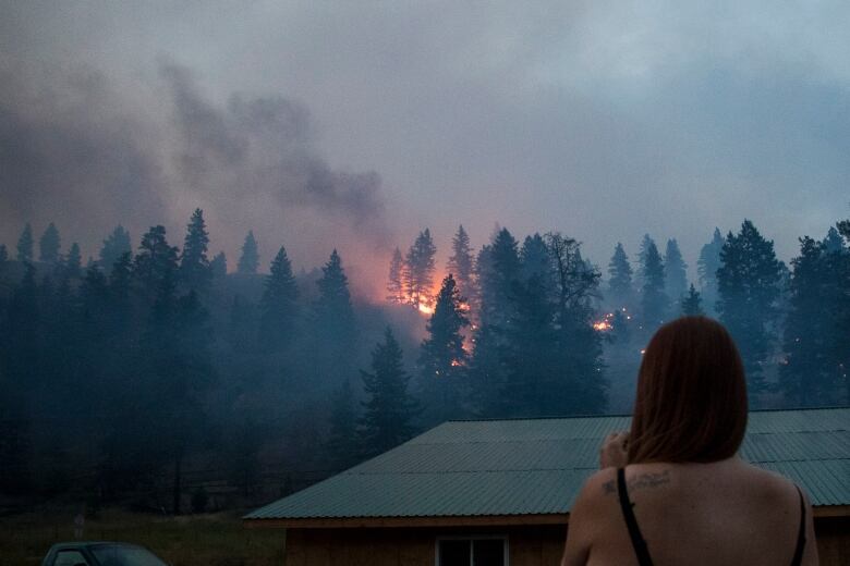 A woman looks out at a wildfire at dusk.