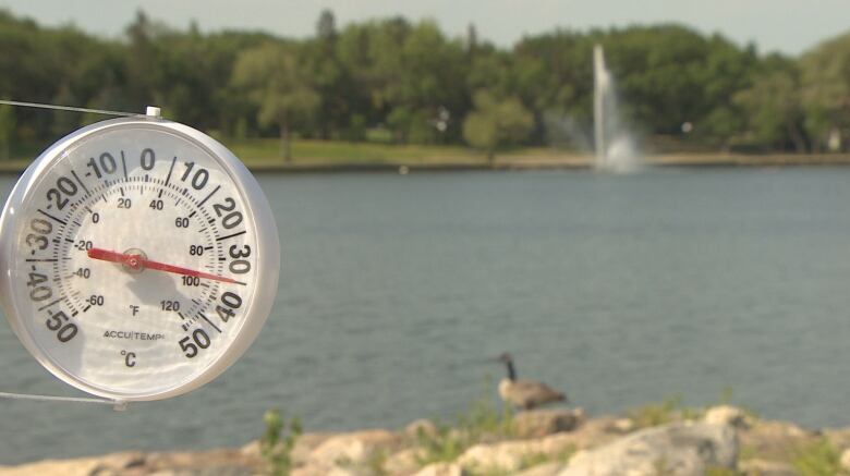 A thermometer reading over 30 degrees sits next to a lake.