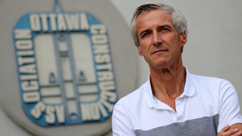 A man stands in front of a sign with the logo of the organization he leads.