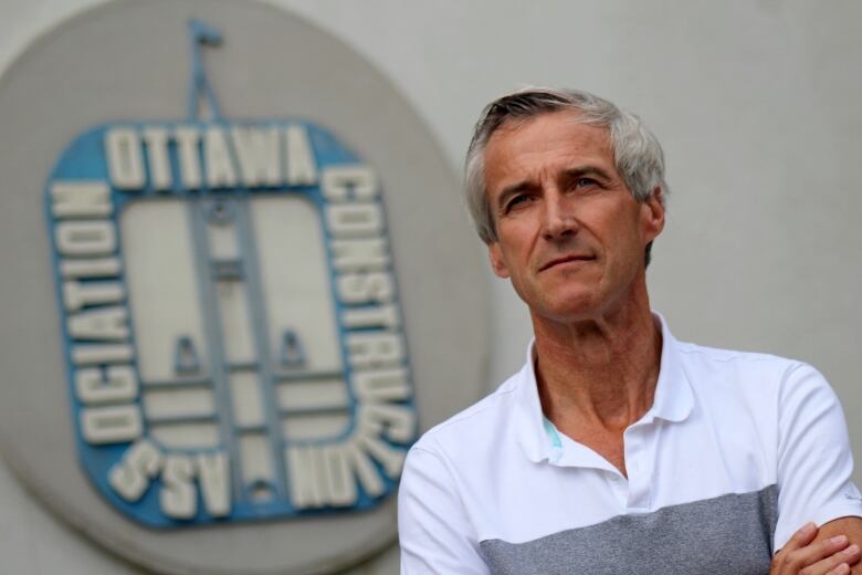 A man stands in front of a sign with the logo of the organization he leads.