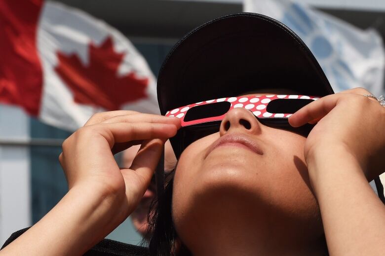 woman holding cardboard solar glasses looks at the sun