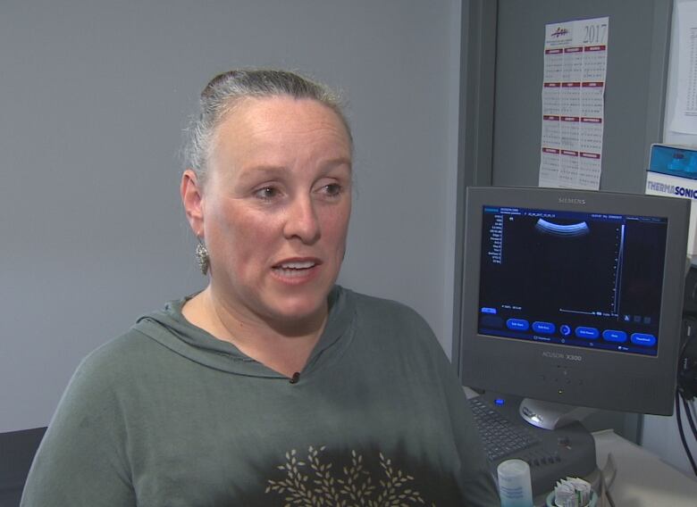 A woman stands in front of an ultrasound machine. Her grey hair is tied back.