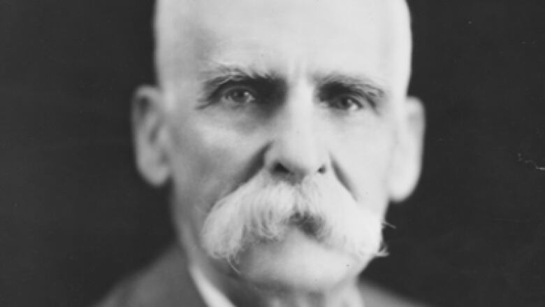 A black and white photograph of a man with a large white mustache. 