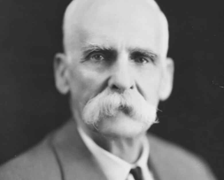 A black and white photograph of a man with a large white mustache. 