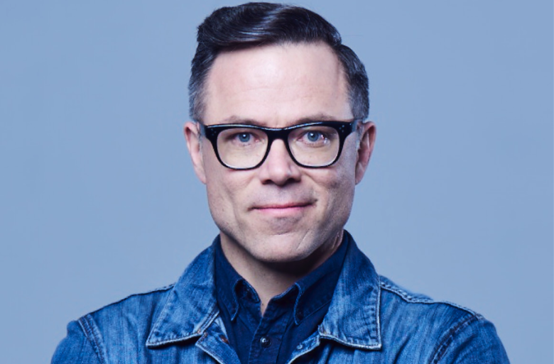 A man wearing glasses in a jean jacket looking at the camera.