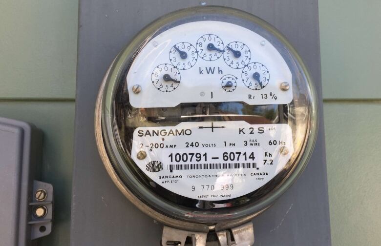 An electric meter is shown close up on the side of a house in daylight.