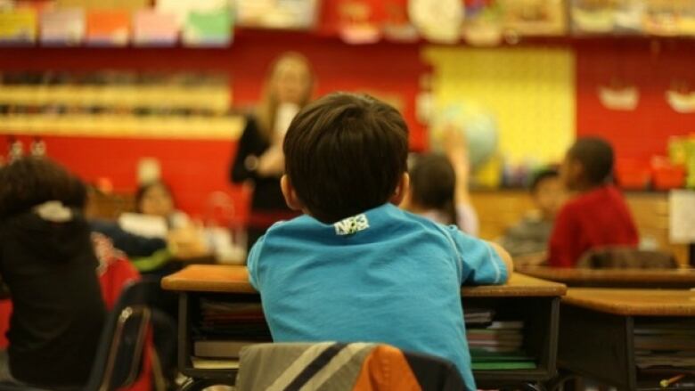 A kid sitting in a classroom. Only his back is seen.