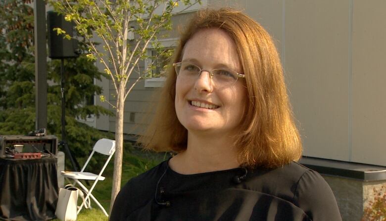 President and CEO of the Calgary Housing Company Sarah Woodgate smiles in an outdoor setting. A home of some sort is behind her.