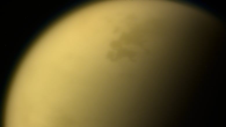 An orange-yellow cloud-shrouded moon hangs in the blackness of space.