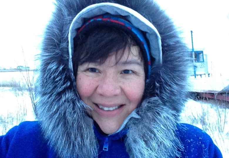 A woman in a park with a fur-lined hood smiles as she stands in the snow.