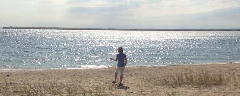 A boy plays on a beach of a sparkling lake.