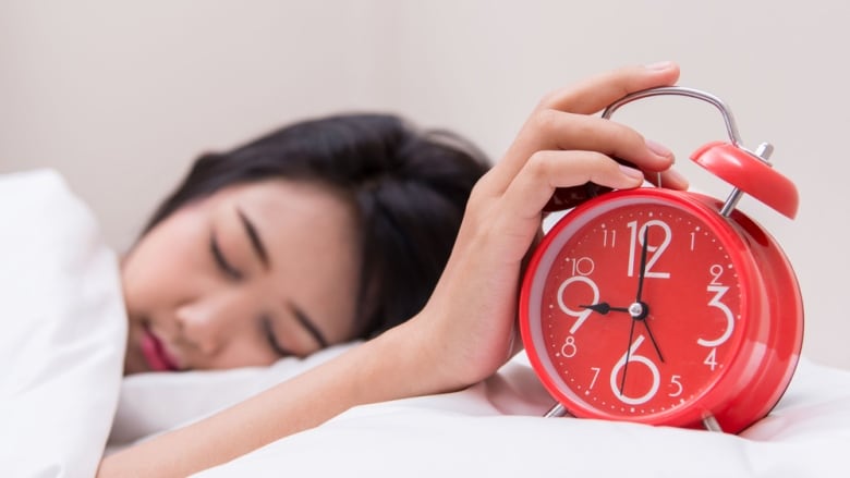 Sleepy young woman reaching out to clock.