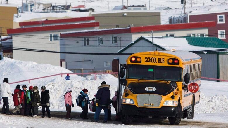 Children board a yellow school bus in the winter.