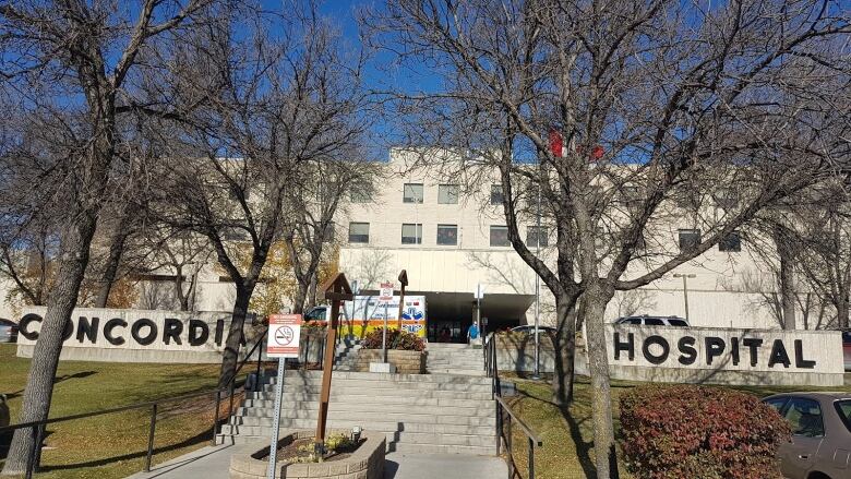 Exterior view of the front of a building with the words Concordia Hospital in big letters on concrete walls.