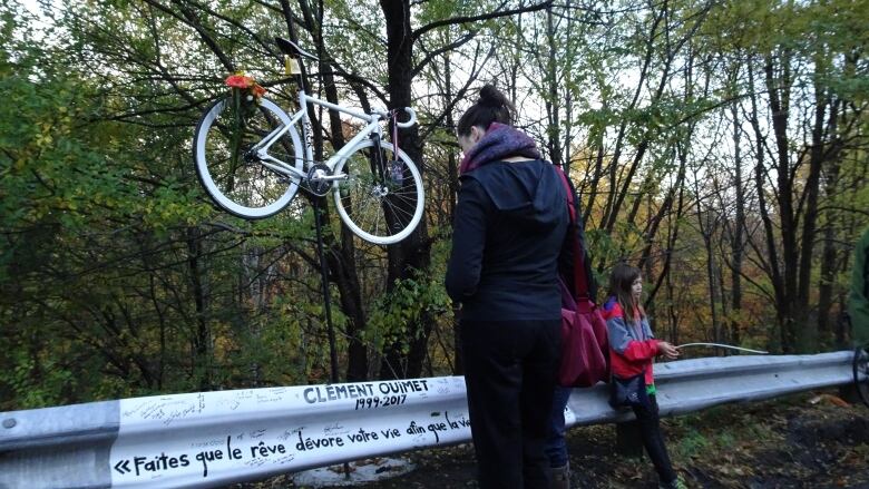 A person bows her head in front of a makeshift memorial, including a white bike. 