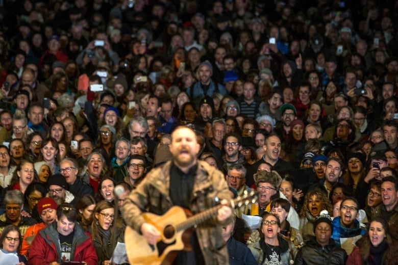 A concert crowd sings in unison behind a guitar player on stage.