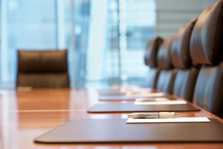 Notepads and pens are placed on a boardroom table surrounded by five empty seats.