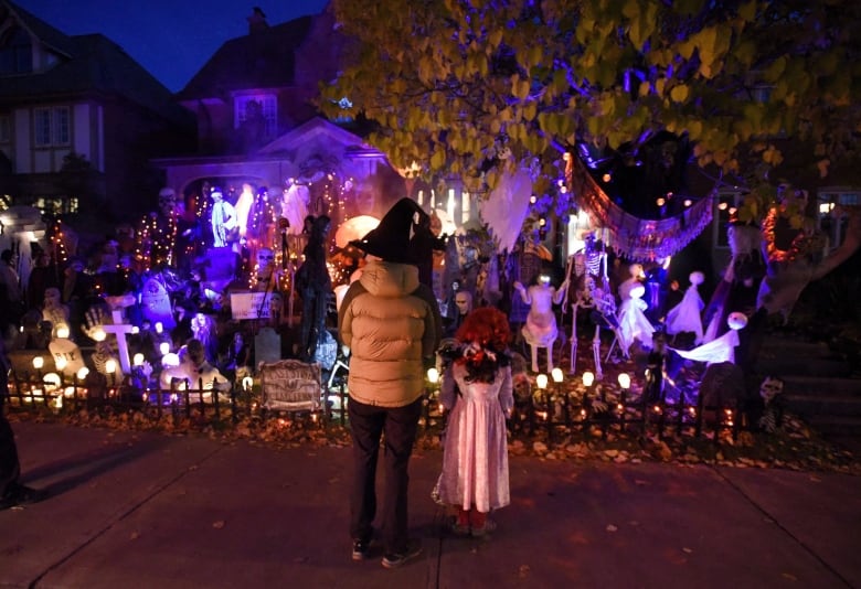 Two people stand in front of a house decked out in a Halloween display. 