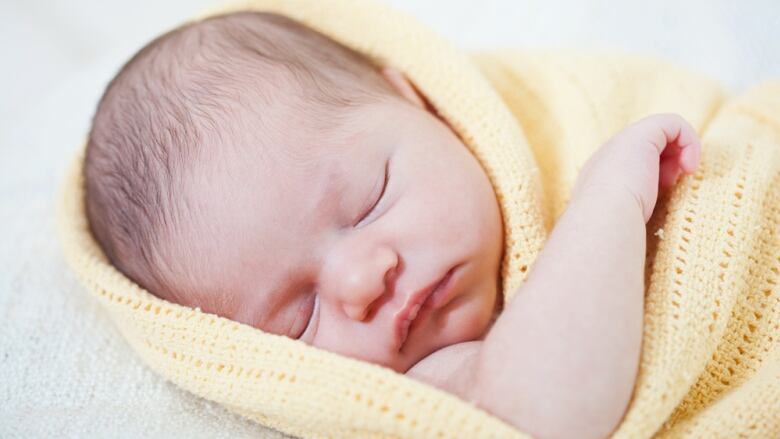 Close up of a sleeping baby swaddled in a yellow blanket.