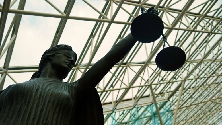 A photo of a statue of Lady Justice with the ceiling of the B.C. Supreme Court in the background. 