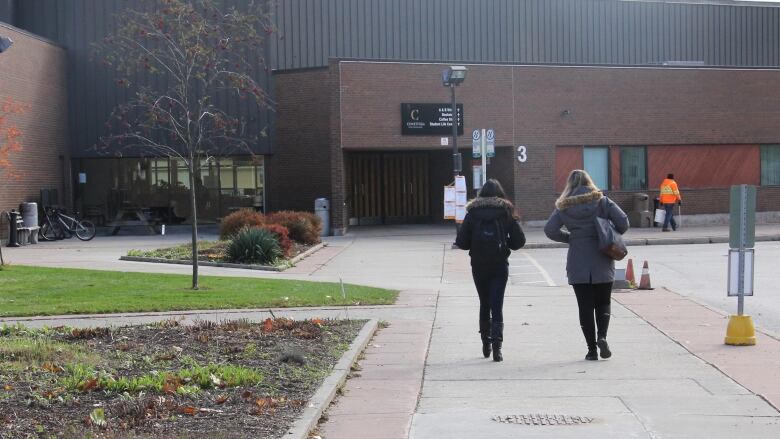 Two people walk away from the camera on a sidewalk on a college campus