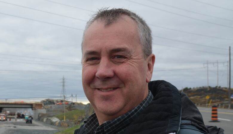 A middle-aged man smiling while a road is under construction behind him.