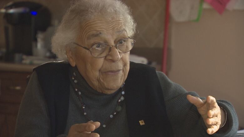 An older Black woman with grey hair wearing a green turtleneck