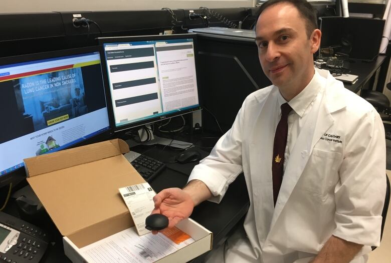 Goodarzi poses with radon kit while sitting in an office