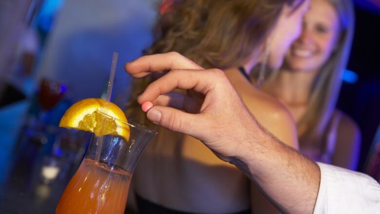 A hand holds a pill over a cocktail. 