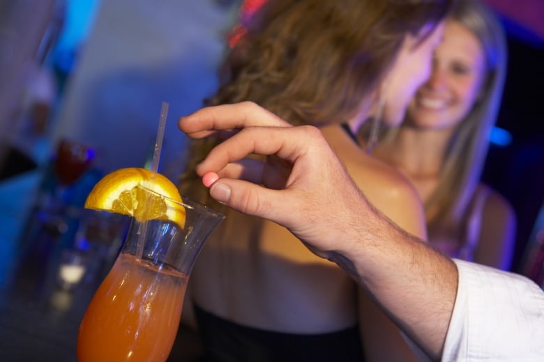 A hand holds a pill over a cocktail. 