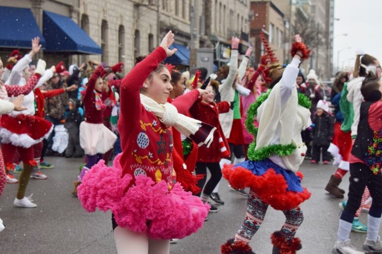 Young dancers wearing brightly coloured outfits dance during a parade with a bit of snow in the air