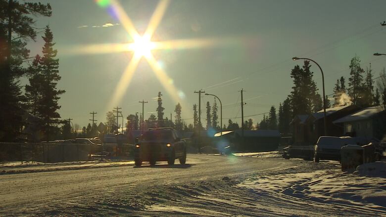 A view of a truck driving down a residential street with the sun low on the horizon.